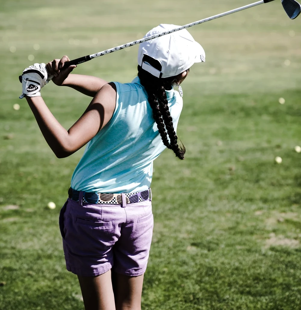A junior golfer completing a golf swing on an open course